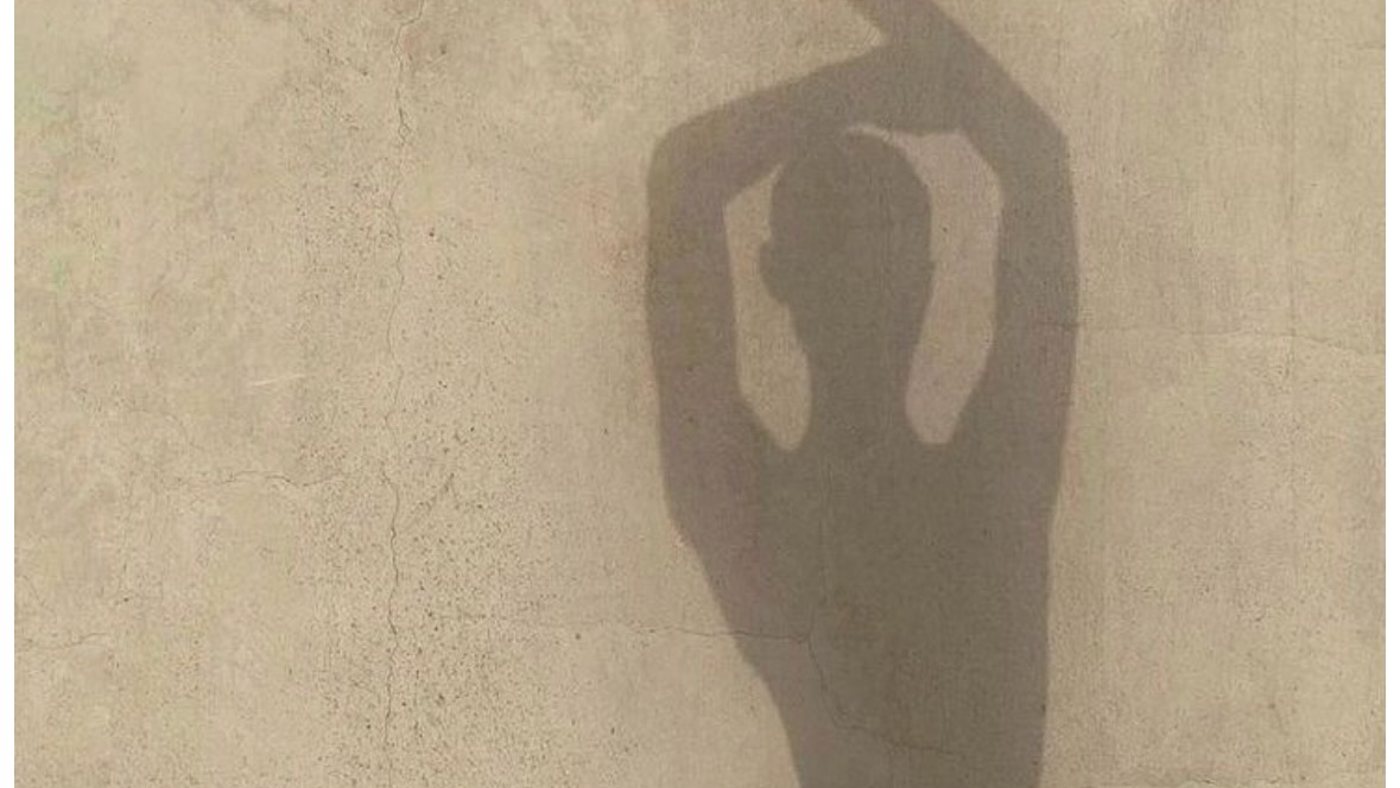 A shadow of a woman with her arms raised on a sunlit wall