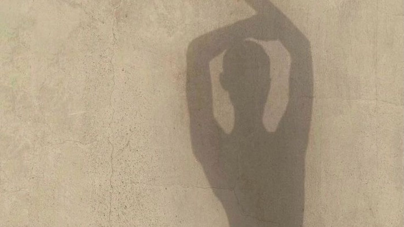 A silhouette with arms raised, cast onto a textured wall