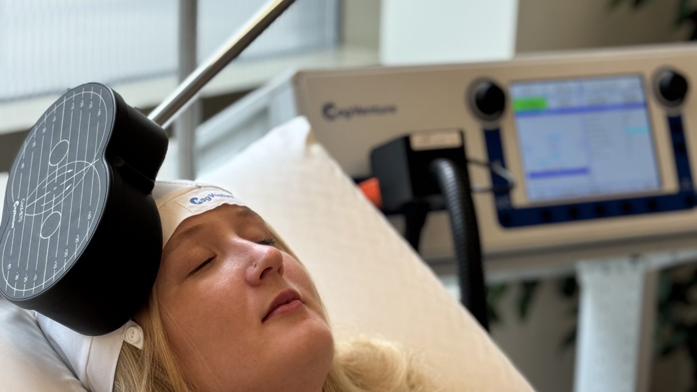 A woman lying on a treatment bed with an rTMS coil positioned beside her head