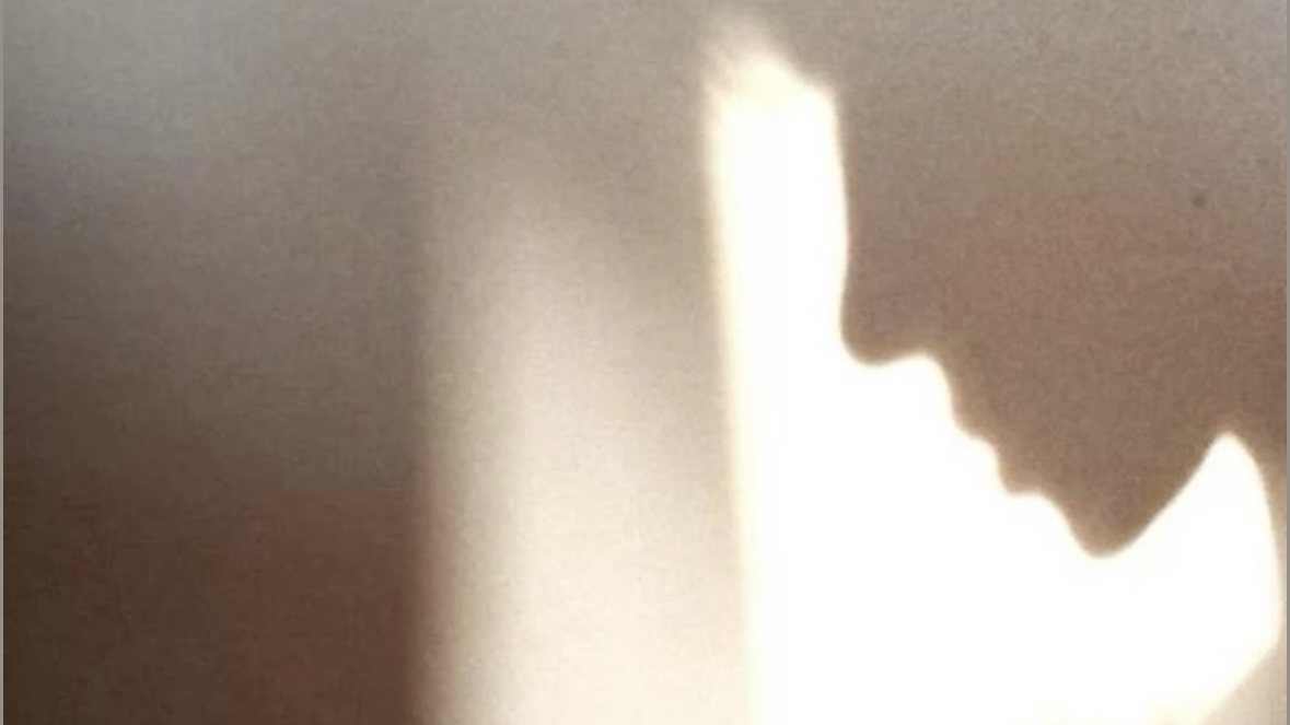 A person’s bowed head in silhouette beside a softly lit wall