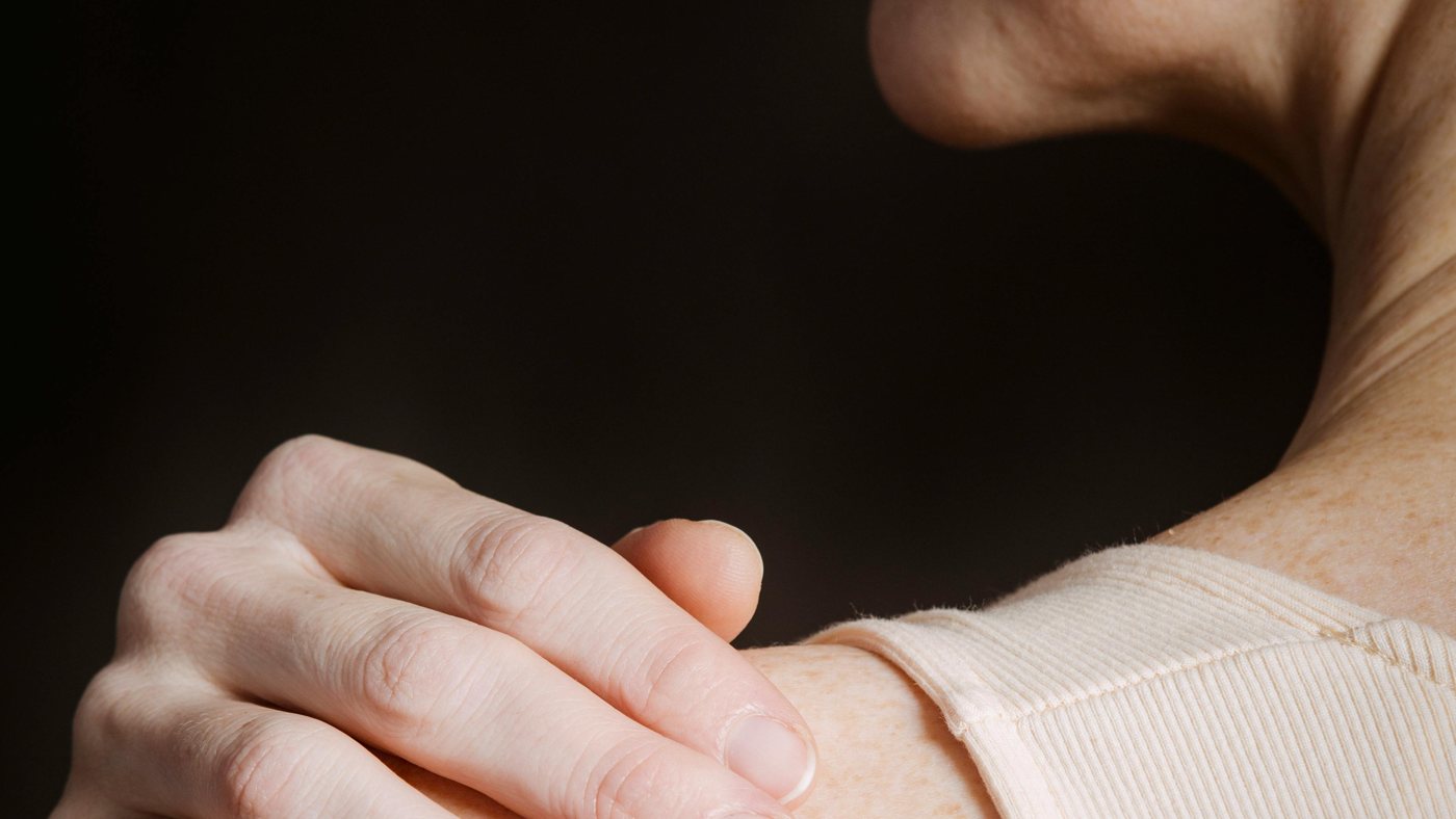 A woman resting a hand on her sore shoulder in soft warm light