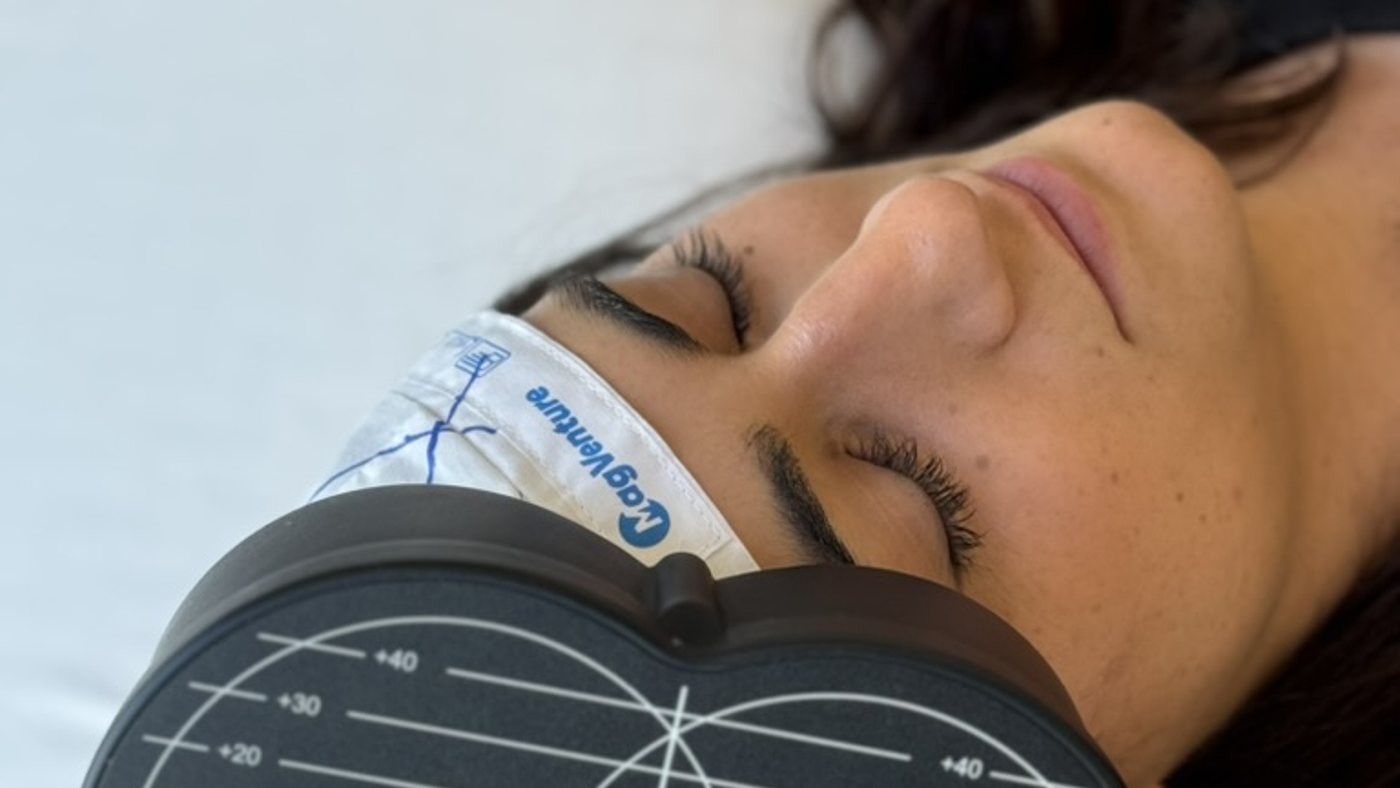 A woman lying on a treatment bed with an rTMS coil positioned beside her head